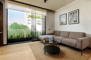 A modern living room with a beige sofa, a glass coffee table, and a large sliding glass door leading to a balcony with greenery. - w Fabulous 1BR With Elegant Balcony in Roma Nte (Mexico City)