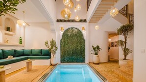A pool area with a green herringbone wall, a green sofa, and hanging lights. - Riad Imrani - swimming pool - 6 mn from Jamaa Al Fna (Marrakech)