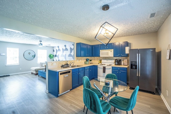 A modern kitchen with blue cabinets, stainless steel appliances, and a glass dining table with teal chairs. - 2br each w/ private full bath (Raleigh)