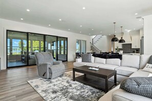A modern living room with a sofa, armchair, and coffee table, a staircase, and a kitchen area. - New Build Baileys Harbor-sunset view & pool table (Baileys Harbor)