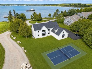 A large white house with a tennis court, surrounded by trees and a lake. - New Build Baileys Harbor-sunset view & pool table (Baileys Harbor)