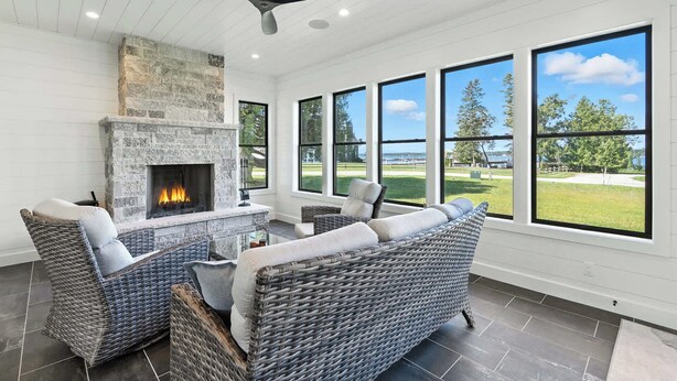Ein Zimmer mit Kamin aus Stein, Korbmöbeln und großen Fenstern mit Blick auf einen Golfplatz.