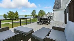 Eine Terrasse mit Gartenmöbeln, Blick auf einen See und ein Wohngebäude im Hintergrund.