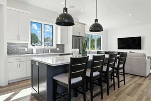 A modern kitchen with a central island, bar stools, a dining area, and a living room with a TV. - New Build Baileys Harbor-sunset view & pool table (Baileys Harbor)