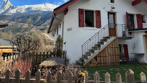 A two-story building with a staircase leading to a balcony, set against a backdrop of snow-capped mountains. - Le Nevada - Duplex T4  Proche Centre (Chamonix-Mont-Blanc)