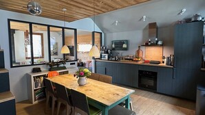 A modern kitchen with a wooden table, chairs, and a large window. - Le Nevada - Duplex T4  Proche Centre (Chamonix-Mont-Blanc)