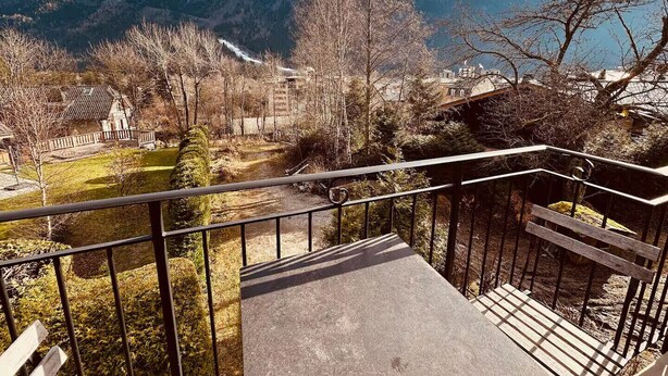 A balcony with a view of snow-capped mountains, a pathway, and a building with a traditional roof. - Le Nevada - Duplex T4  Proche Centre (Chamonix-Mont-Blanc)