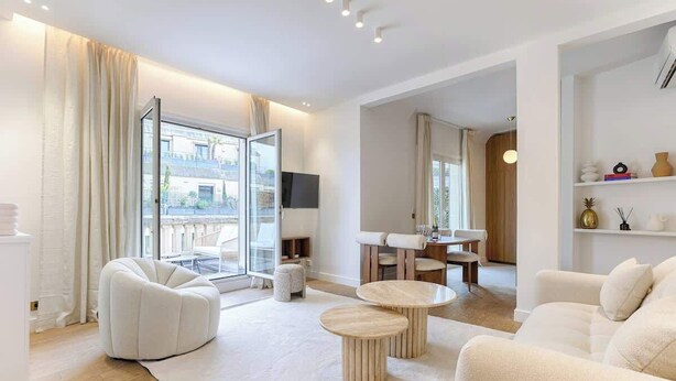 A modern living room with a sofa, two round coffee tables, a glass door leading to a balcony, and a dining area with a table and chairs. - Appartement de Luxe avec terrasse Champs Elysées (Paris)