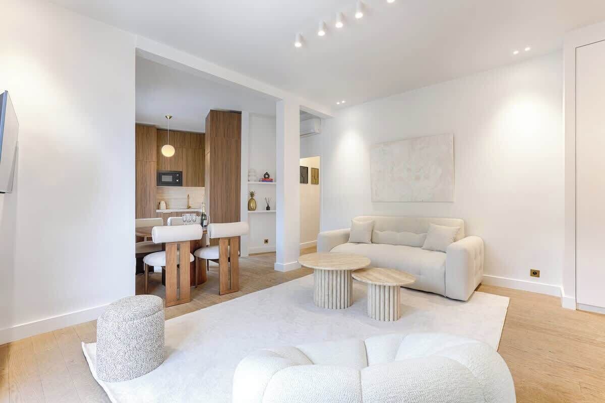 Een moderne woonkamer met een bank, twee ronde salontafels en een eethoek met een tafel en stoelen.