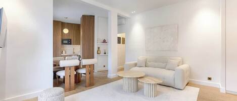 Een moderne woonkamer met een bank, twee ronde salontafels en een eethoek met een tafel en stoelen.