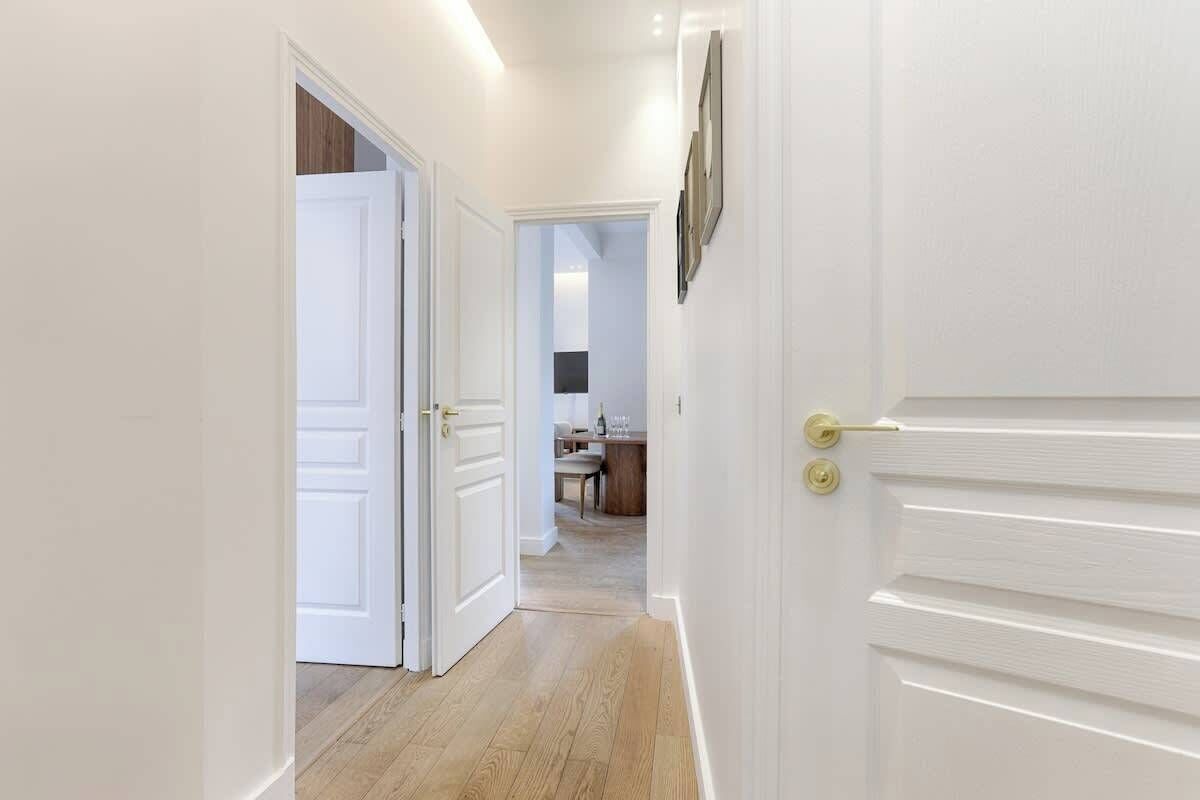 A hallway with white doors, wooden flooring, and a framed picture on the wall.