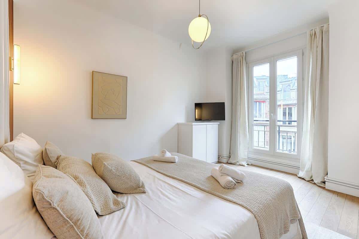 Et hotelværelse med en stor seng, et fladskærms-tv, et vindue med gardiner og et billede på væggen.