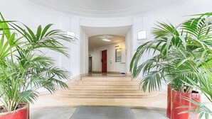 A grand entrance with a marble staircase, potted plants, and a red door leading to a hallway. - Appartement de Luxe avec terrasse Champs Elysées (Paris)