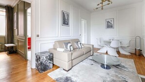Een moderne woonkamer met een beige bank, een marmeren salontafel en een eethoek met witte stoelen.
