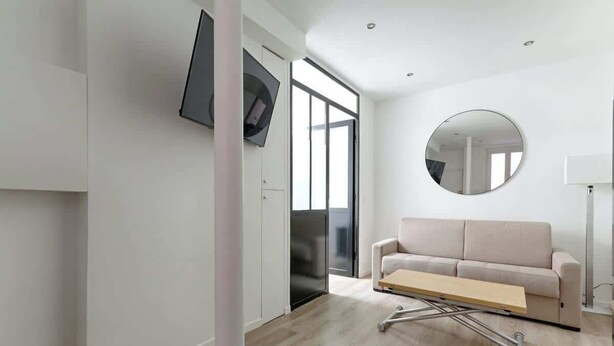 Una sala de estar moderna con un sofá, un televisor de pantalla plana montado en la pared, un espejo redondo y una mesa extensible.
