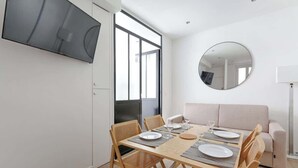 Una sala de estar moderna con comedor, un televisor de pantalla plana en la pared, un espejo redondo y un sofá.