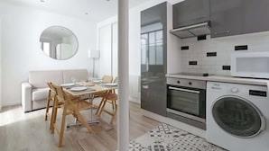 Cocina moderna con horno empotrado, microondas y lavadora. Zona de comedor con mesa y sillas.
