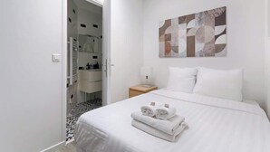 Habitación de hotel con cama, mesita de noche, una obra de arte en la pared y un baño visible a través de una puerta abierta.