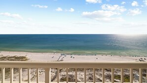 A beach view from a balcony with a railing, sandy beach, and ocean.