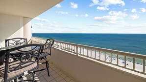 A balcony with a table and chairs, overlooking a beach with a clear sky.