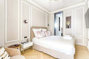 Un dormitorio ordenado con una cama grande, mesitas de noche, una silla y una pequeña mesa.