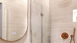 Een moderne badkamer met een douchecabine van glas, een ronde spiegel, een gouden kraan en een handdouche.