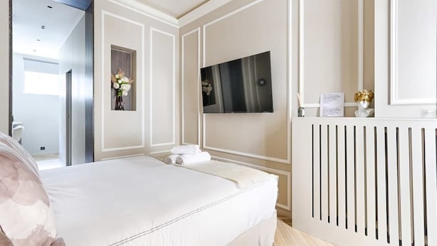 Hotelkamer met een bed, een aan de muur bevestigde televisie, een radiator en een deur naar een andere kamer.