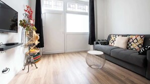 Een moderne woonkamer met een grijze bank, een ronde salontafel en een aan de muur bevestigde televisie.