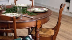 Een eetgedeelte met een ronde houten tafel gedekt voor twee personen, omringd door houten stoelen met geweven zittingen.