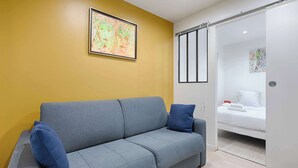 A modern room with a grey sofa, a yellow accent wall, and a bed with white bedding. - Bastille/Republique Charming & Cosy Apartment 1BR (Paris)