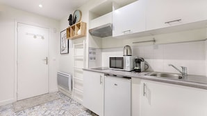 A kitchen with white cabinets, a microwave, a kettle, and a sink. - Bastille/Republique Charming & Cosy Apartment 1BR (Paris)