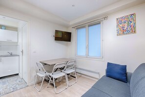 A compact living space with a kitchenette, a dining area with a table and chairs, a sofa, a TV, and a large window.