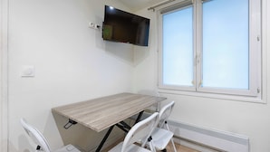 A room with a table, chairs, a TV mounted on the wall, and a window. - Bastille/Republique Charming & Cosy Apartment 1BR (Paris)
