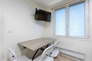 A room with a table, chairs, a TV mounted on the wall, and a window.