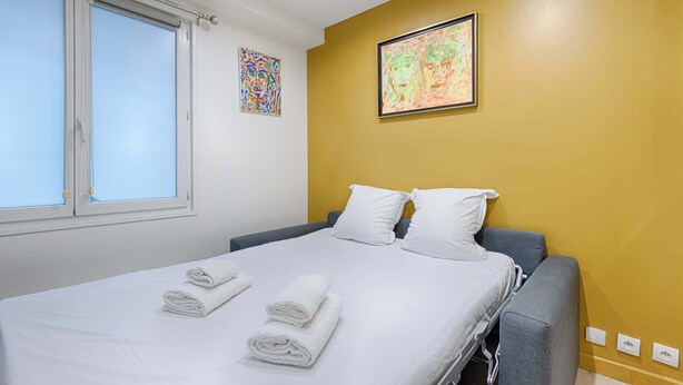 A hotel room with a bed, two pillows, a window, and artwork on the wall. - Bastille/Republique Charming & Cosy Apartment 1BR (Paris)