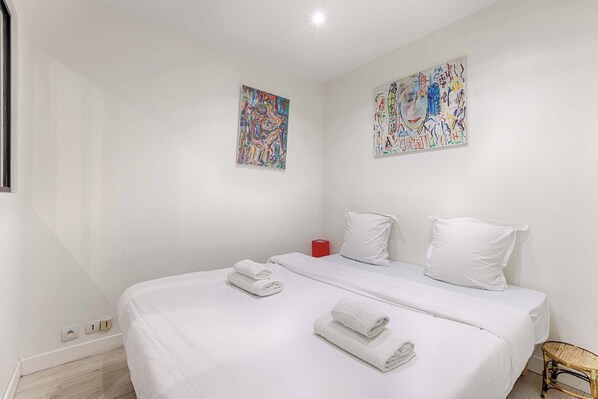A hotel room with a large bed, two pillows, a red cup, and two abstract paintings on the wall.