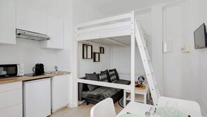 A compact room with a bunk bed, kitchenette, and a dining area. - Appartement de charme cosy au cœur de Batignolles (Paris)