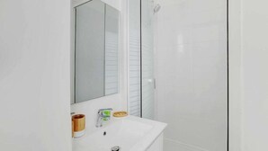 A bathroom with a white sink, a mirror, and a glass shower enclosure. - Appartement de charme cosy au cœur de Batignolles (Paris)
