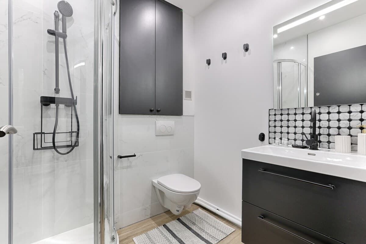 Ein modernes Badezimmer mit einer Duschkabine aus Glas, einer weißen Toilette, einem schwarzen Schrank und einer gefliesten Rückwand.