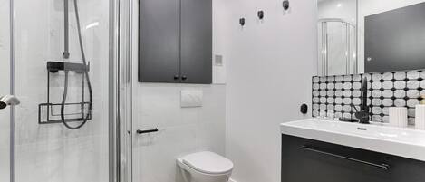 Ein modernes Badezimmer mit einer Duschkabine aus Glas, einer weißen Toilette, einem schwarzen Schrank und einer gefliesten Rückwand.