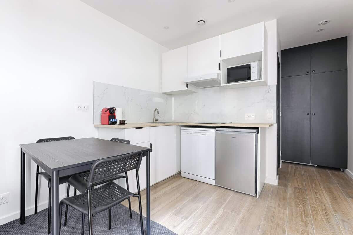 A compact kitchen with white cabinets, a microwave, a dishwasher, and a dark door.