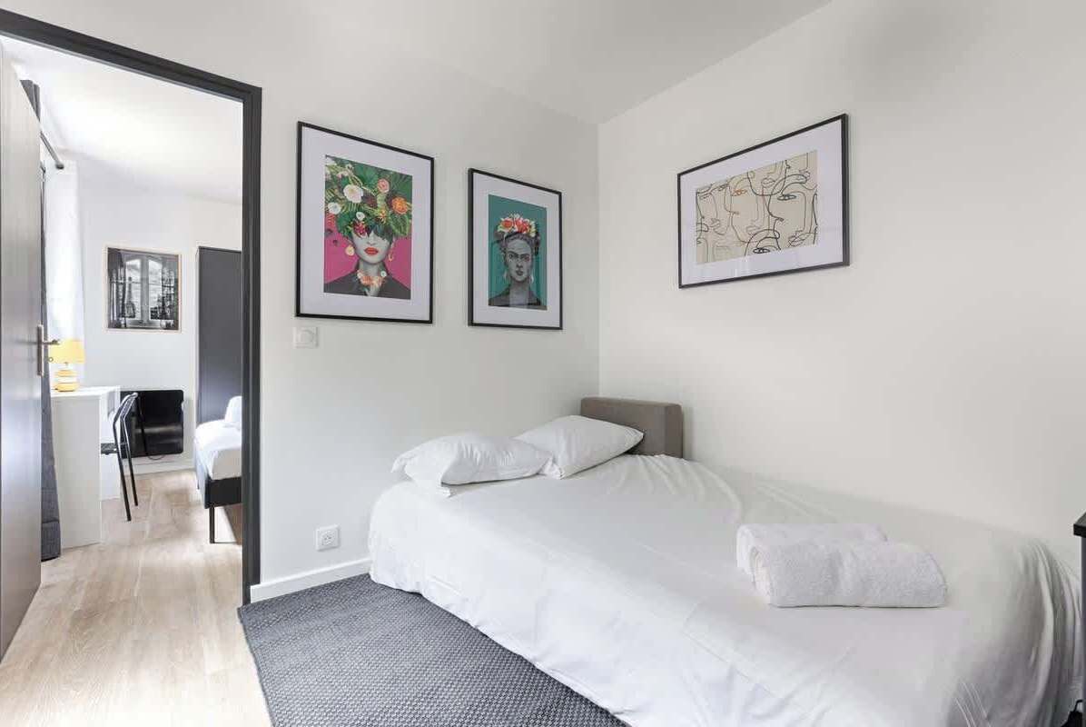Ett modernt hotellrum med en säng, ett skrivbord och två inramade konstverk på väggen.