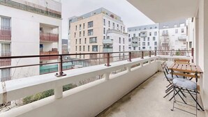 Un balcon avec une table et des chaises, donnant sur un quartier résidentiel avec des immeubles modernes.