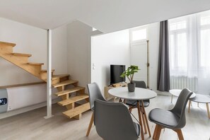Ein stilvolles Wohnzimmer mit einer Holztreppe, einem runden Esstisch mit Stühlen, einem Flachbildfernseher und einem Blumentopf.
