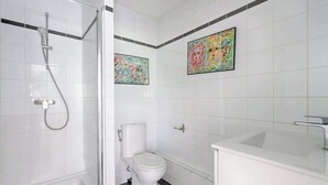 Un baño con cabina de ducha de vidrio, inodoro blanco, lavabo con grifo moderno y dos cuadros abstractos en la pared.