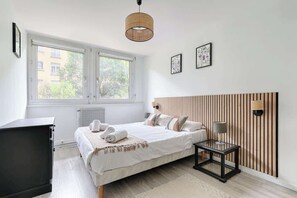 A bedroom with a bed, bedside table, lamp, and a window with a view of buildings. - Beaugrenelle Tour Eiffel II Cosy Apartment 2BR (Paris)