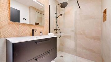 Une salle de bain moderne avec un mur orné d’un motif en chevrons, un grand miroir, un meuble-lavabo aux tons foncés doté de tiroirs et une cabine de douche en verre.