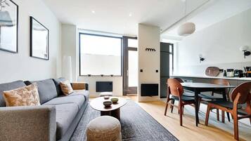 Un salon moderne avec un canapé gris, une table basse ronde et un coin repas comprenant des chaises en bois et une table blanche.