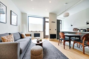 A modern living room with a grey sofa, a round coffee table, and a dining area with wooden chairs and a white table.