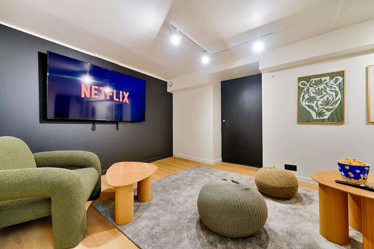 A modern living room with a large flat-screen TV displaying 'NETFLIX', a green sofa, a wooden coffee table, and a popcorn bowl.